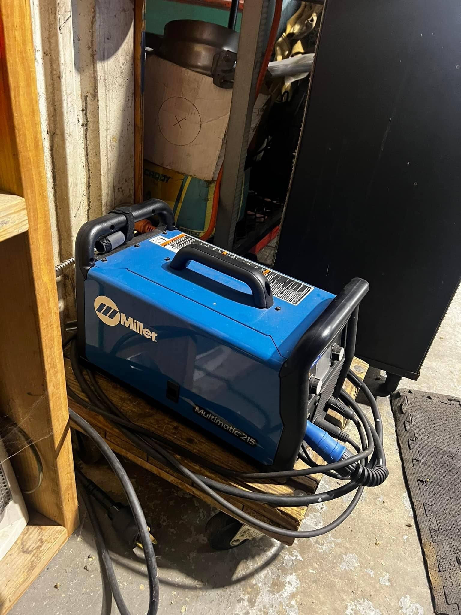 A blue welding machine is sitting on top of a wooden pallet.
