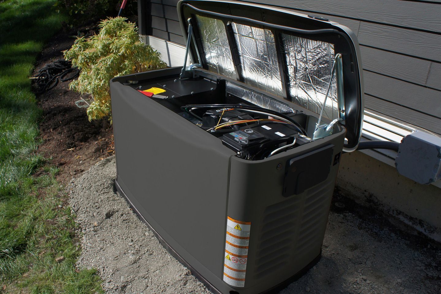 A generator is sitting outside of a house with the lid open.