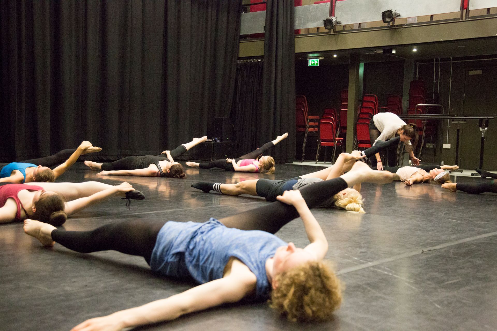 Instructor guiding clients in a stretching class with right leg stretches on the floor to improve muscle elasticity, tone, and range of motion.