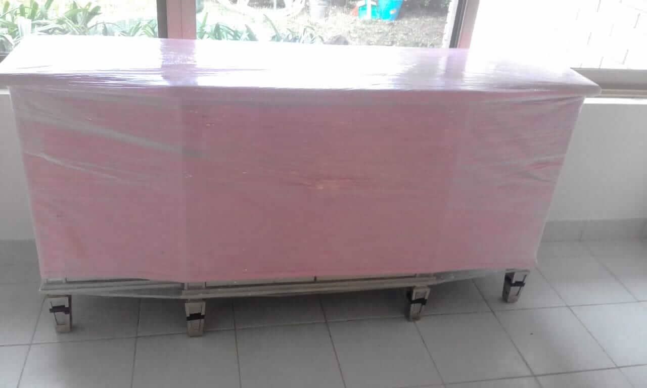 Una mesa rosa con envoltura de plástico encima está frente a una ventana.