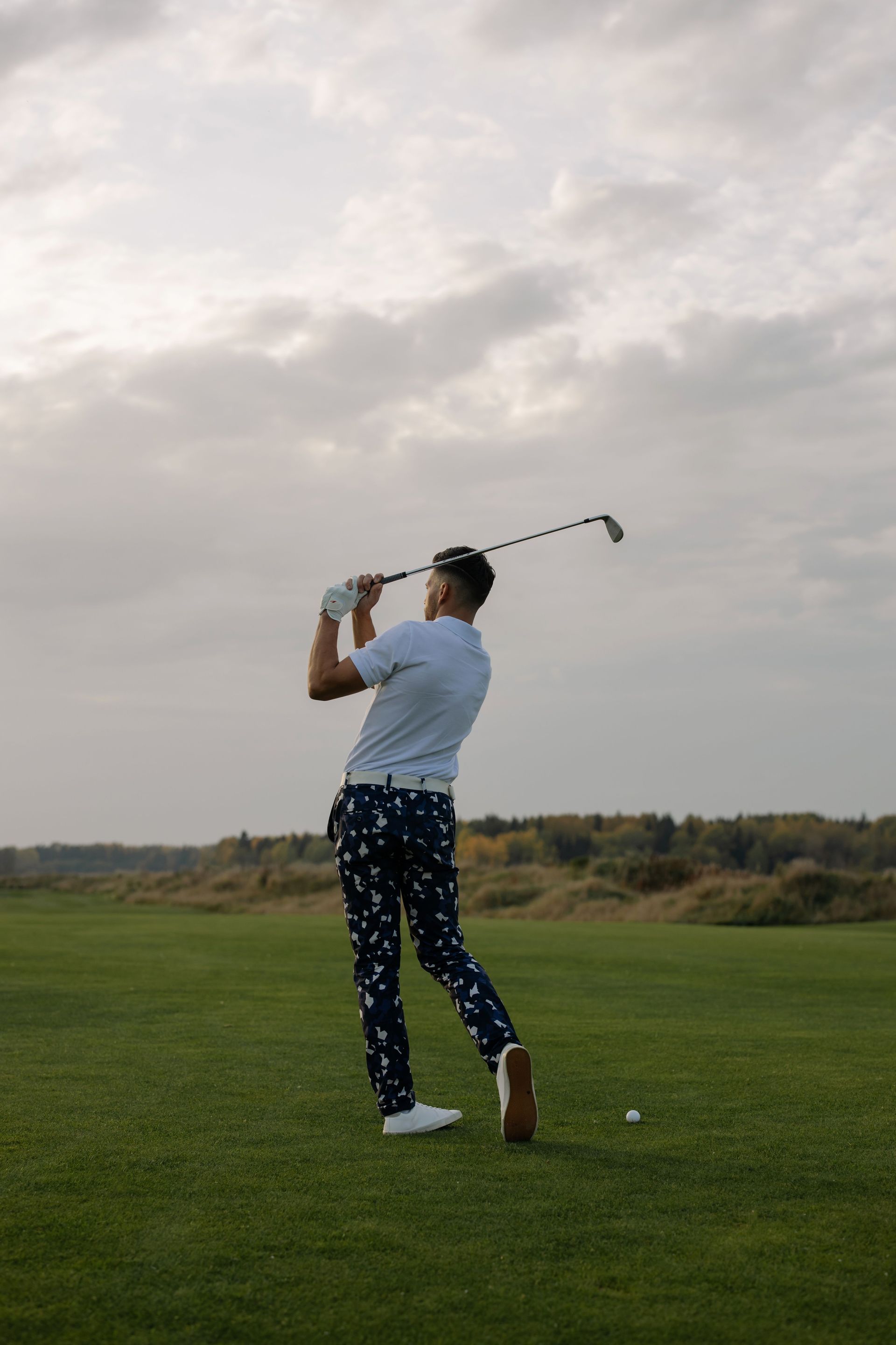 Een golfer midden in zijn swing op een groene fairway onder een bewolkte hemel.