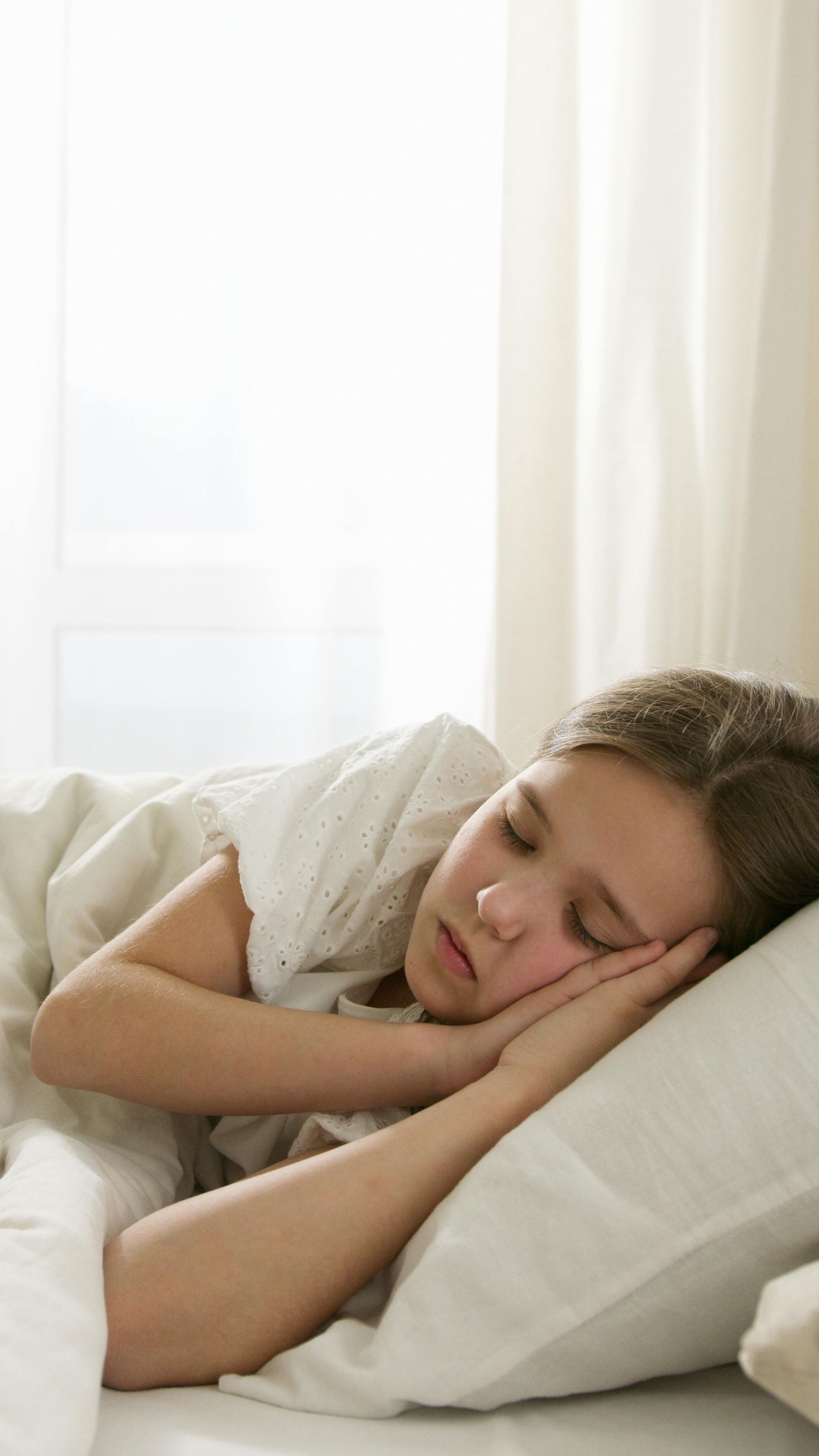 Een persoon slaapt in een lichtgekleurd bed, rustend op witte kussens en lakens.