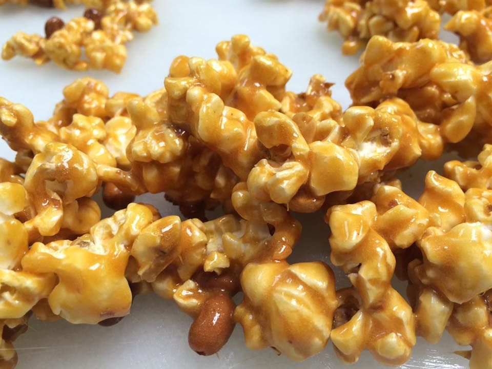 A close up of caramel popcorn with peanuts on a white surface.