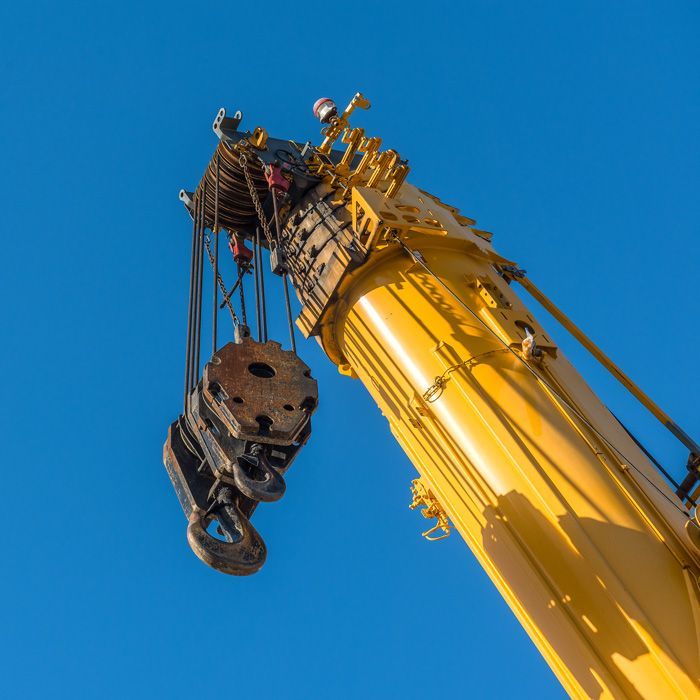 Yellow crane with raised telescopic arm against solid blue sky