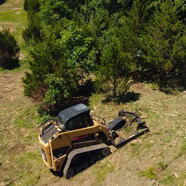 skid steer with attachment clearing wooded area