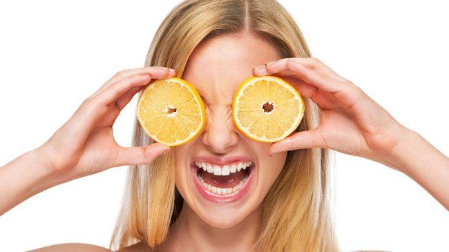 Lachende blonde vrouw die sinaasappelschijfjes als bril voor haar ogen houdt.