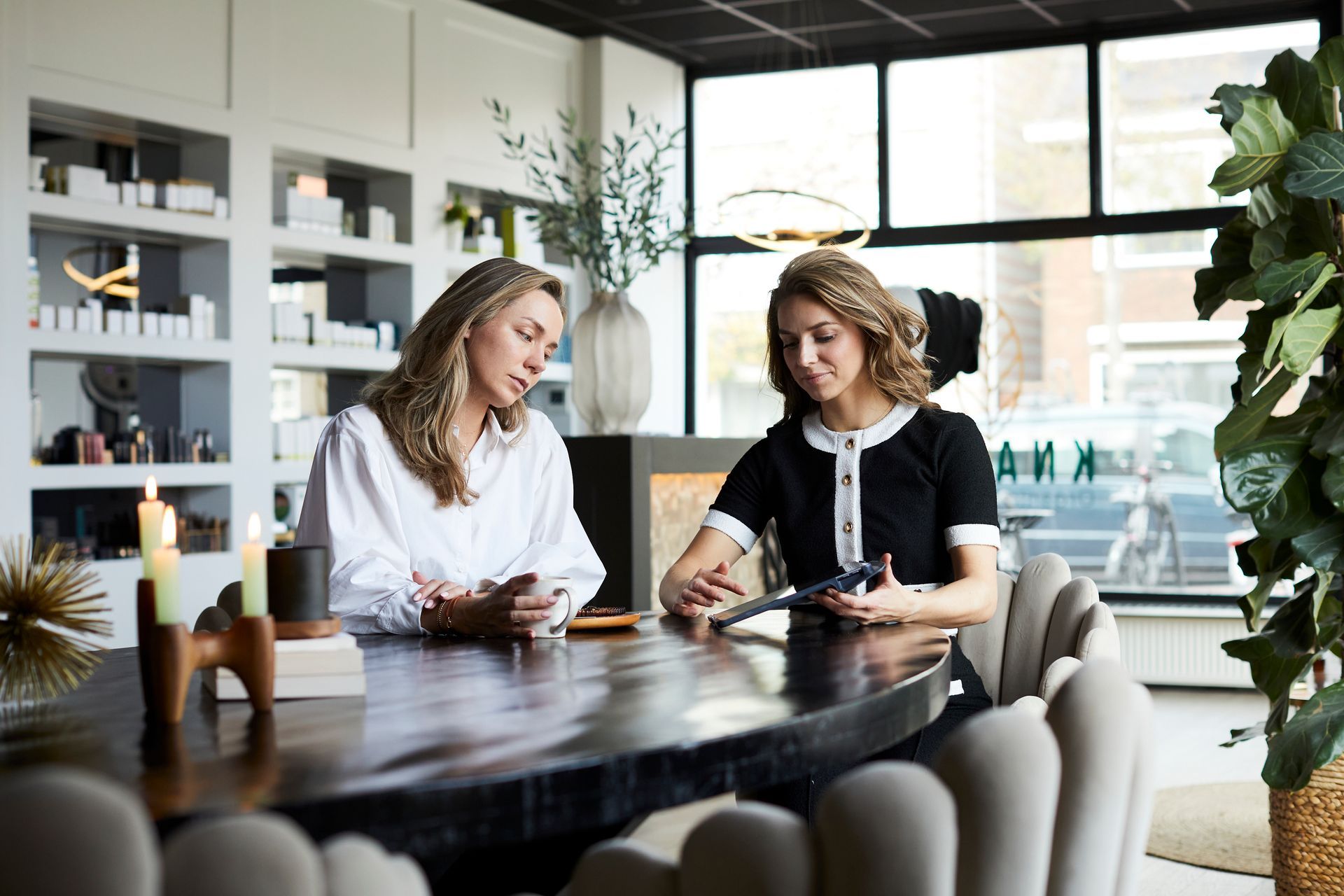 Twee mensen praten bij het drinken van een kop koffie aan een tafel in een lichte kantoorlounge.
