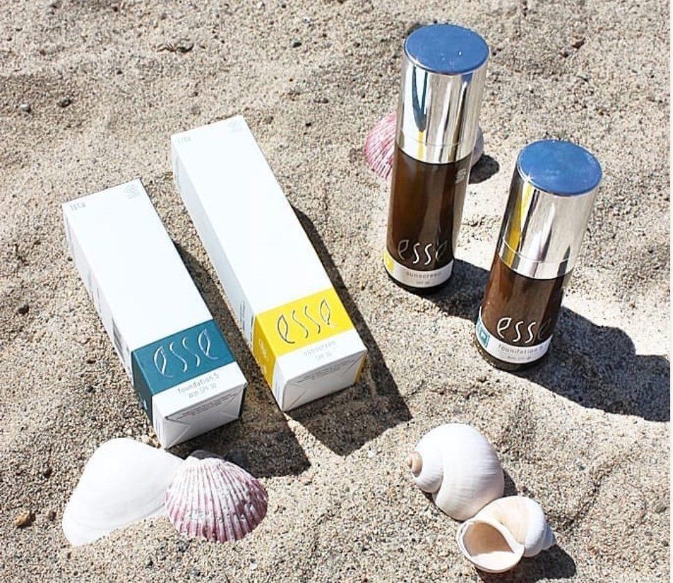 Cosmeticaflessen, doosjes en schelpen uitgestald op het zand.