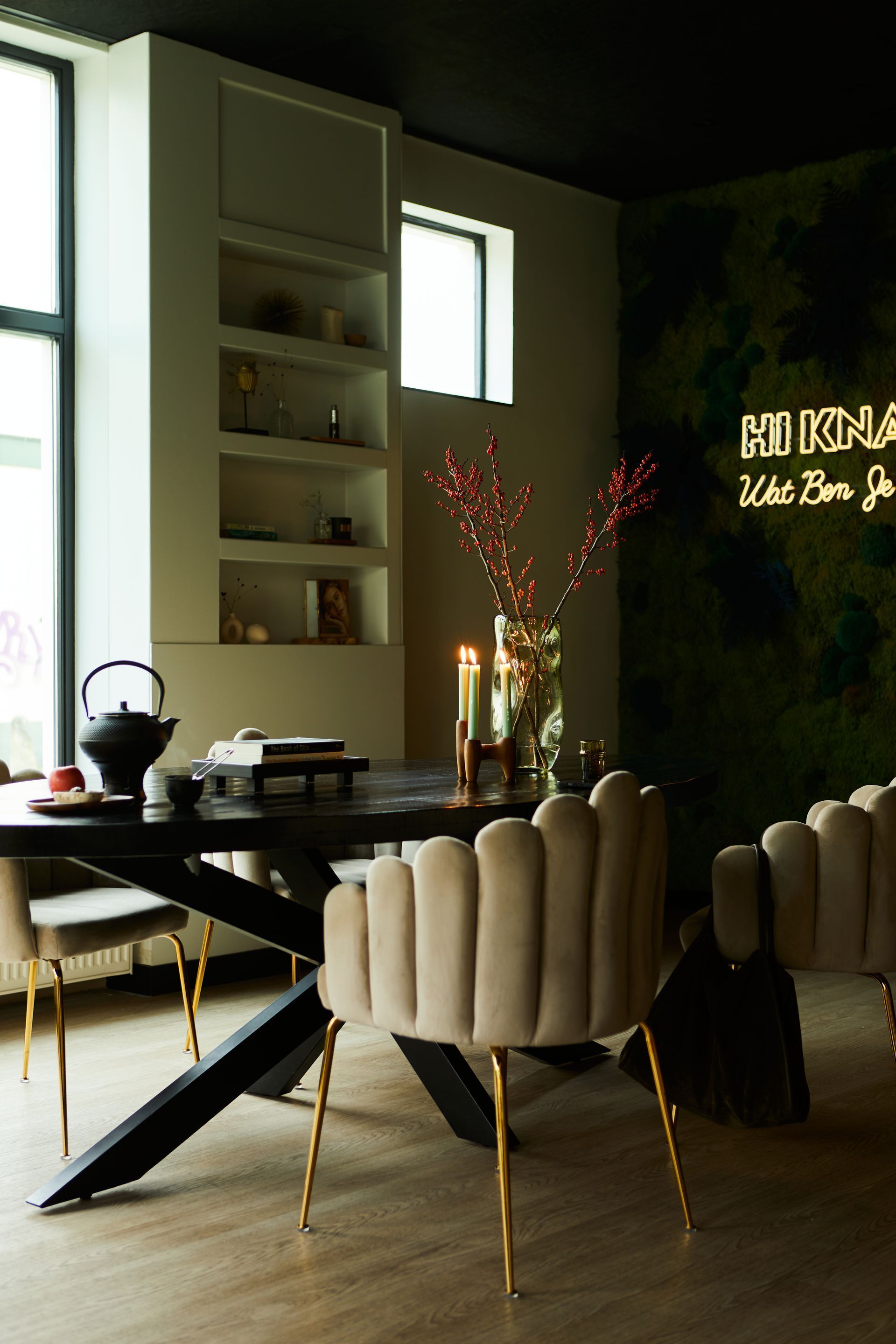 Moderne eetkamer met hoge ramen, een donkere tafel, crèmekleurige stoelen en warme, sfeervolle verlichting.