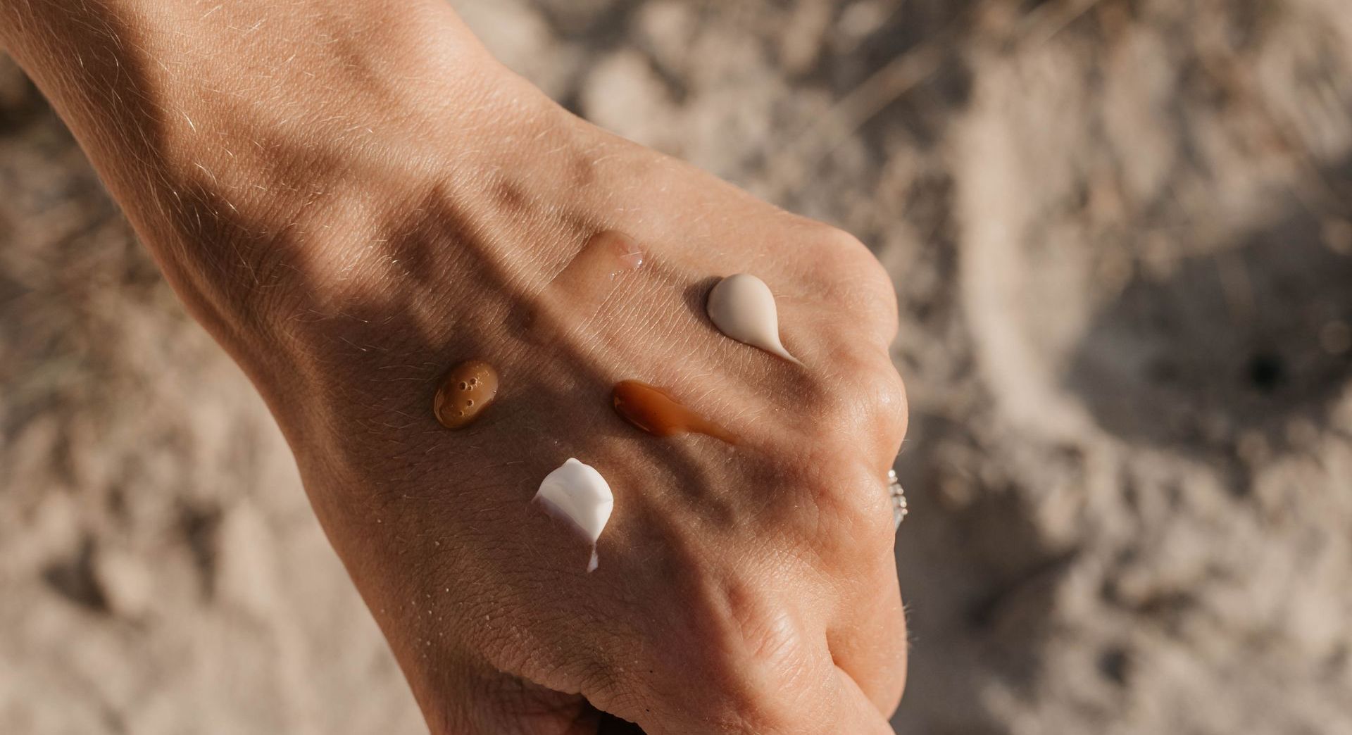 Close-up van een hand die kleine schelpjes vasthoudt op een zanderige ondergrond.