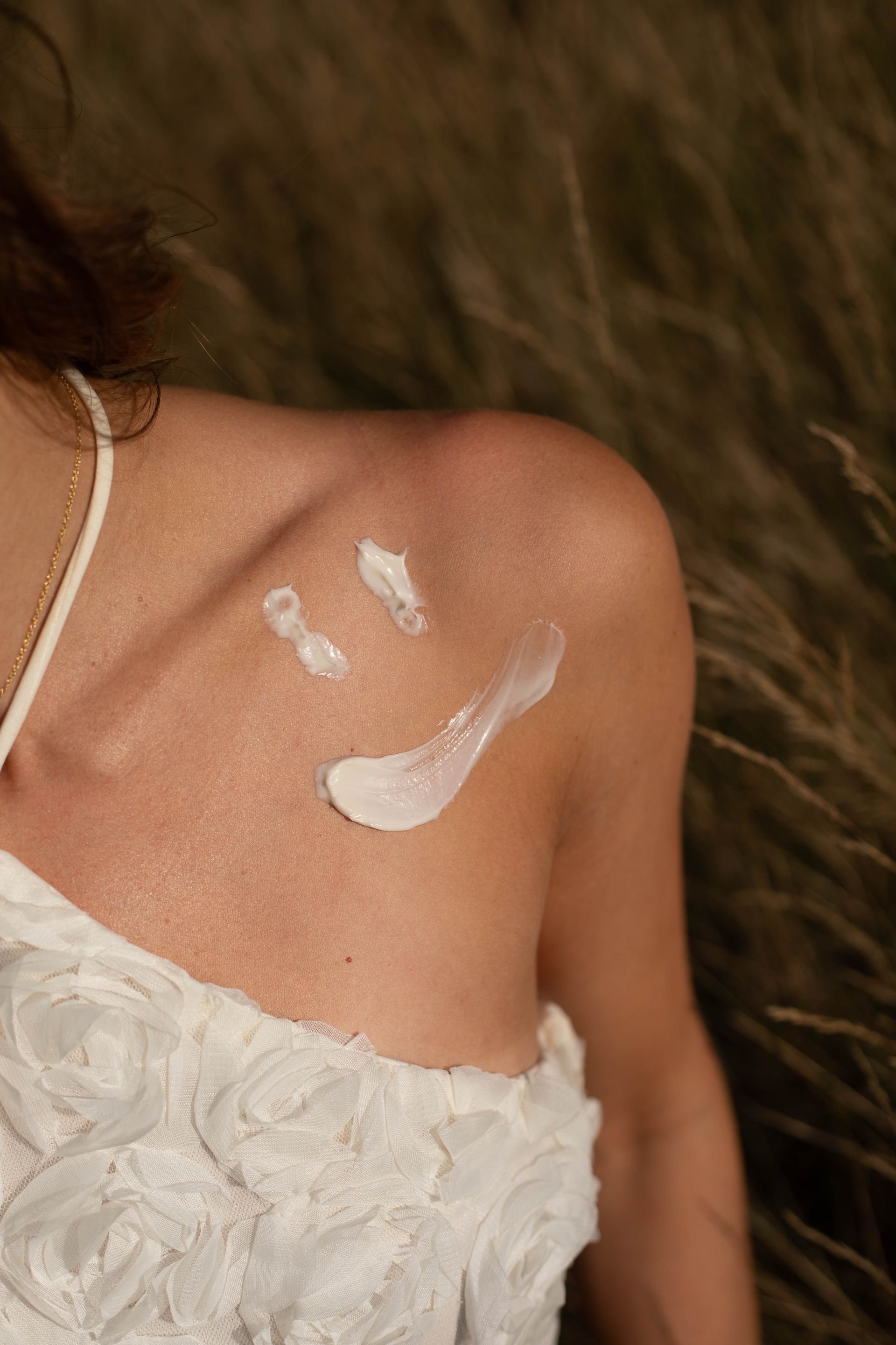Close-up van een schouder in een witte kanten jurk met witte crème- of verfvlekken op de huid.