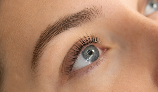 Close-up van een blauw oog met lange wimpers en een gevormde wenkbrauw op een gezicht met een lichte huid.