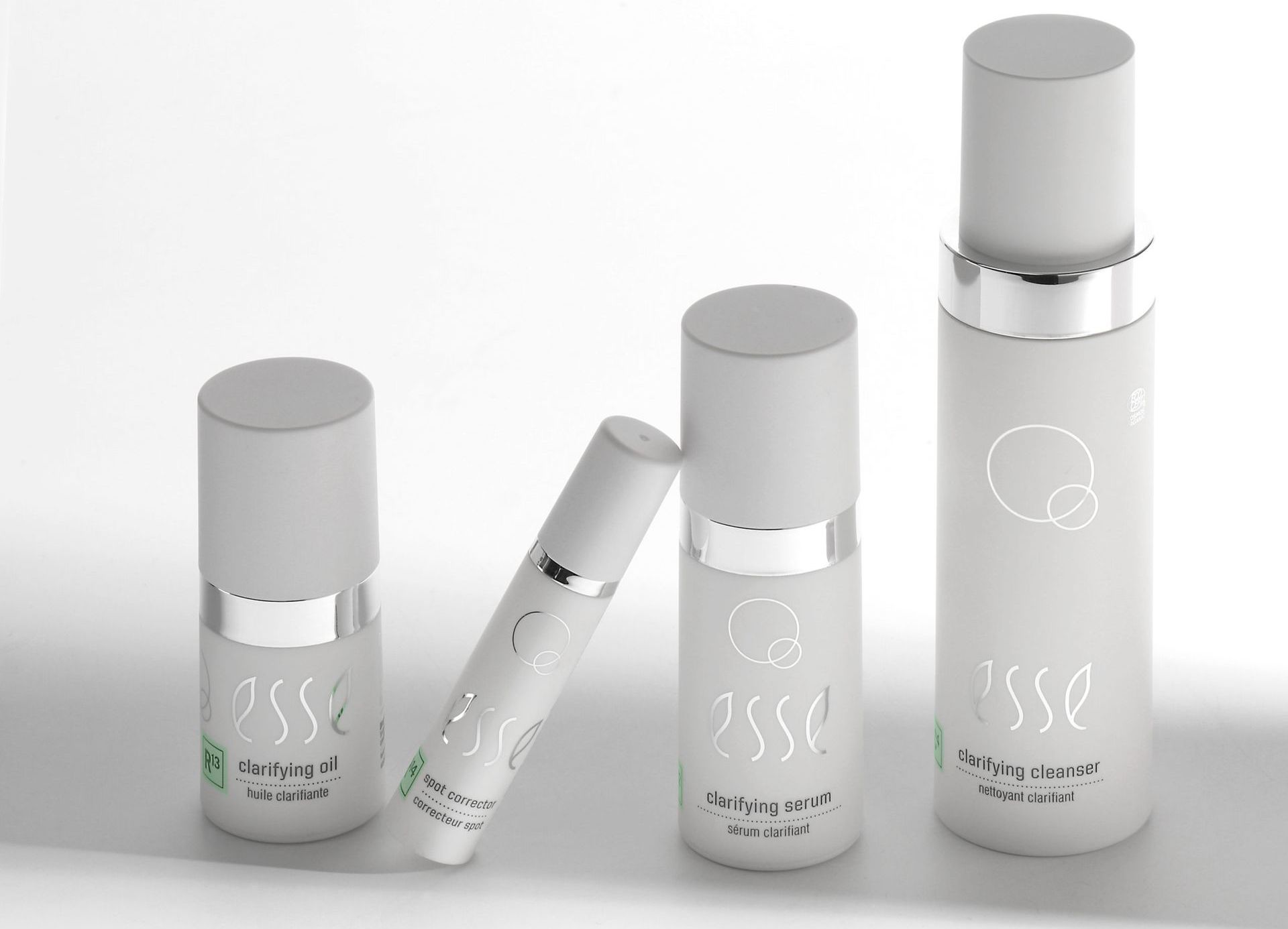 Vier zilverkleurige cosmeticaflesjes en een tube, geplaatst op een witte achtergrond.