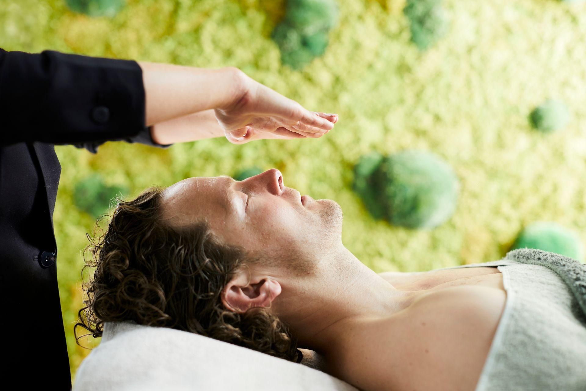 Een persoon krijgt een gezichtsbehandeling terwijl ze op een massagetafel ligt, met een hand boven het gezicht.