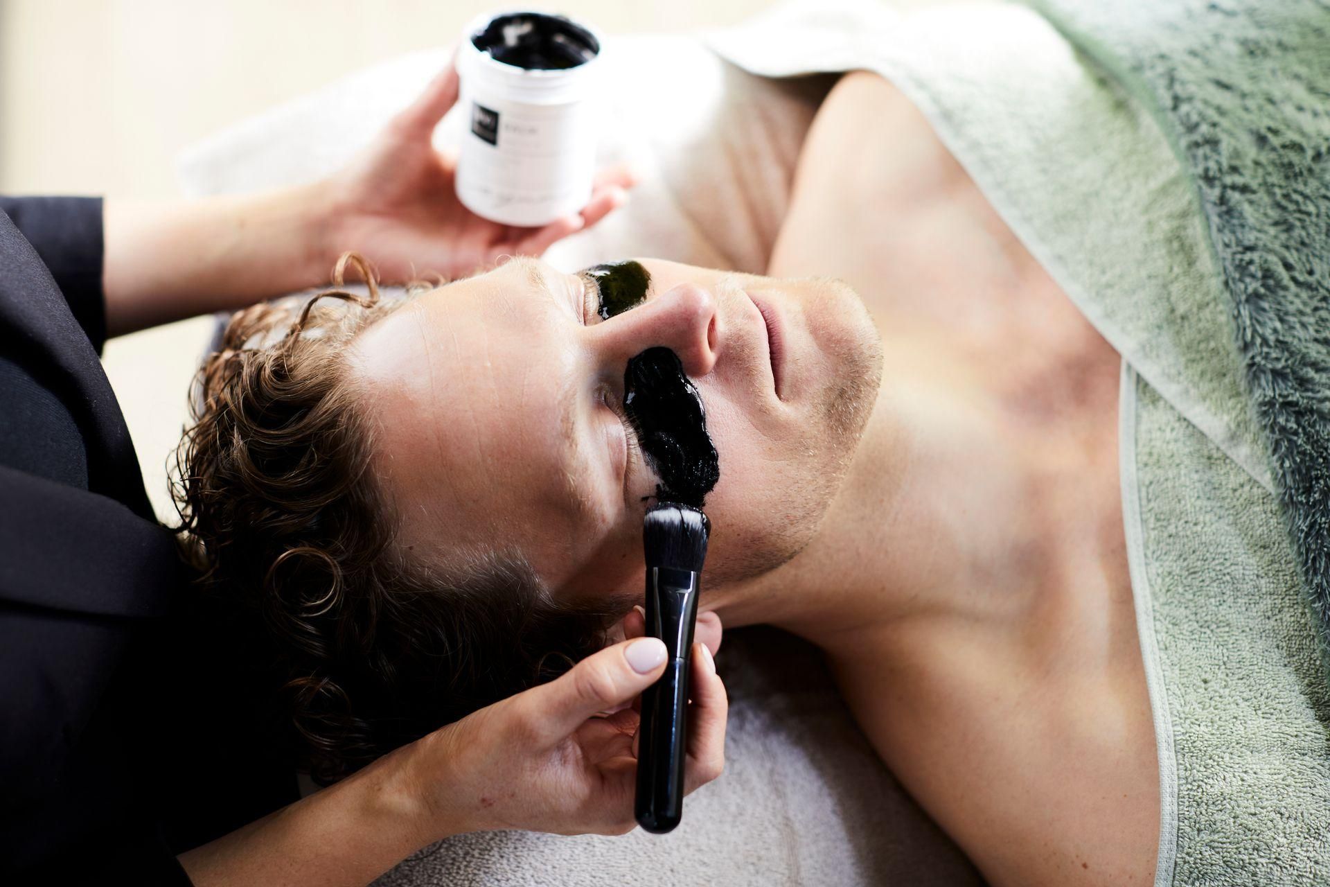 Vrouw krijgt een gezichtsbehandeling met een cosmetische kwast terwijl ze op een spabank ligt.