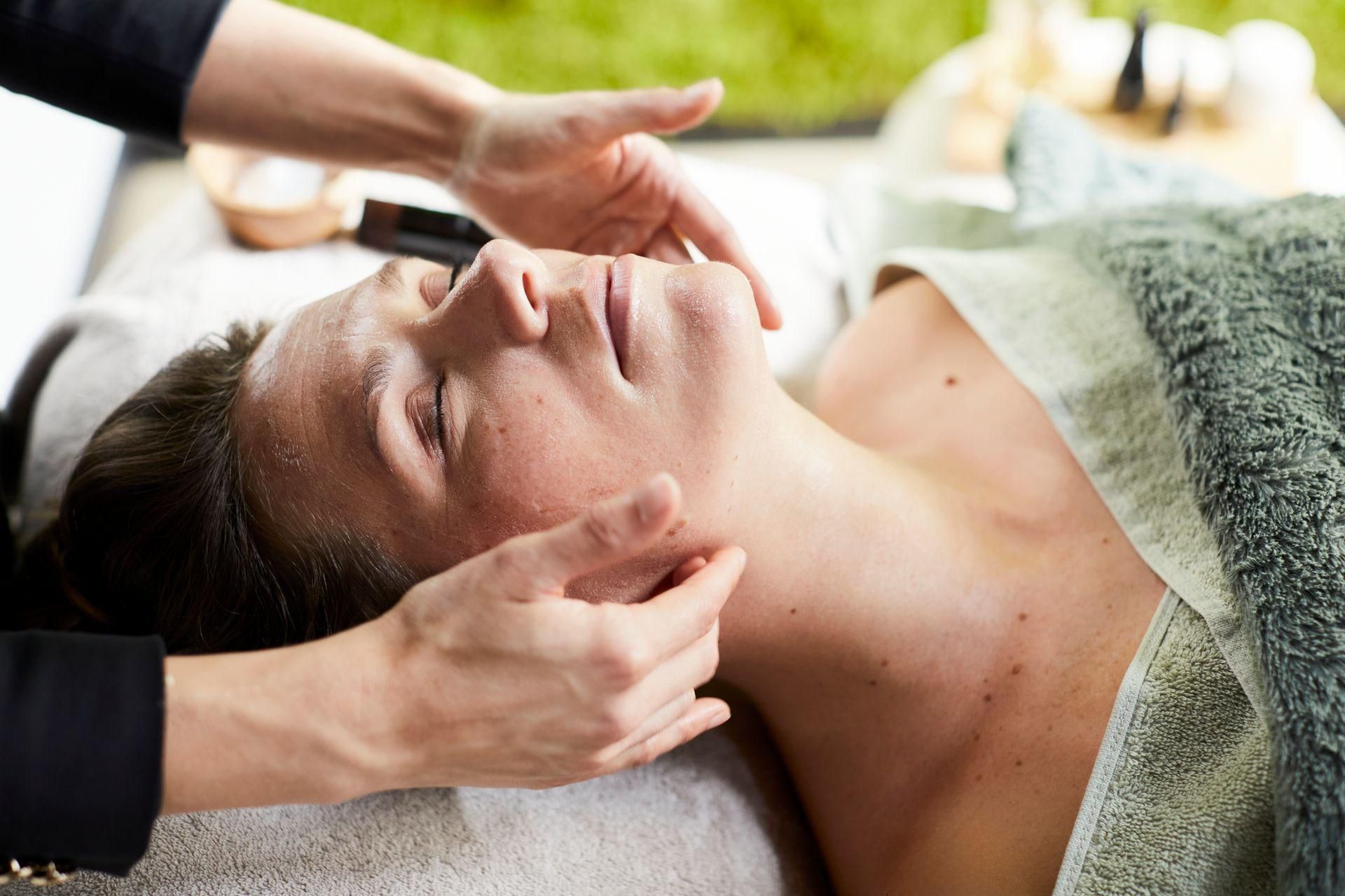 Gezichtsmassage met een vrouw die met gesloten ogen op een behandeltafel ligt in een spa-omgeving.
