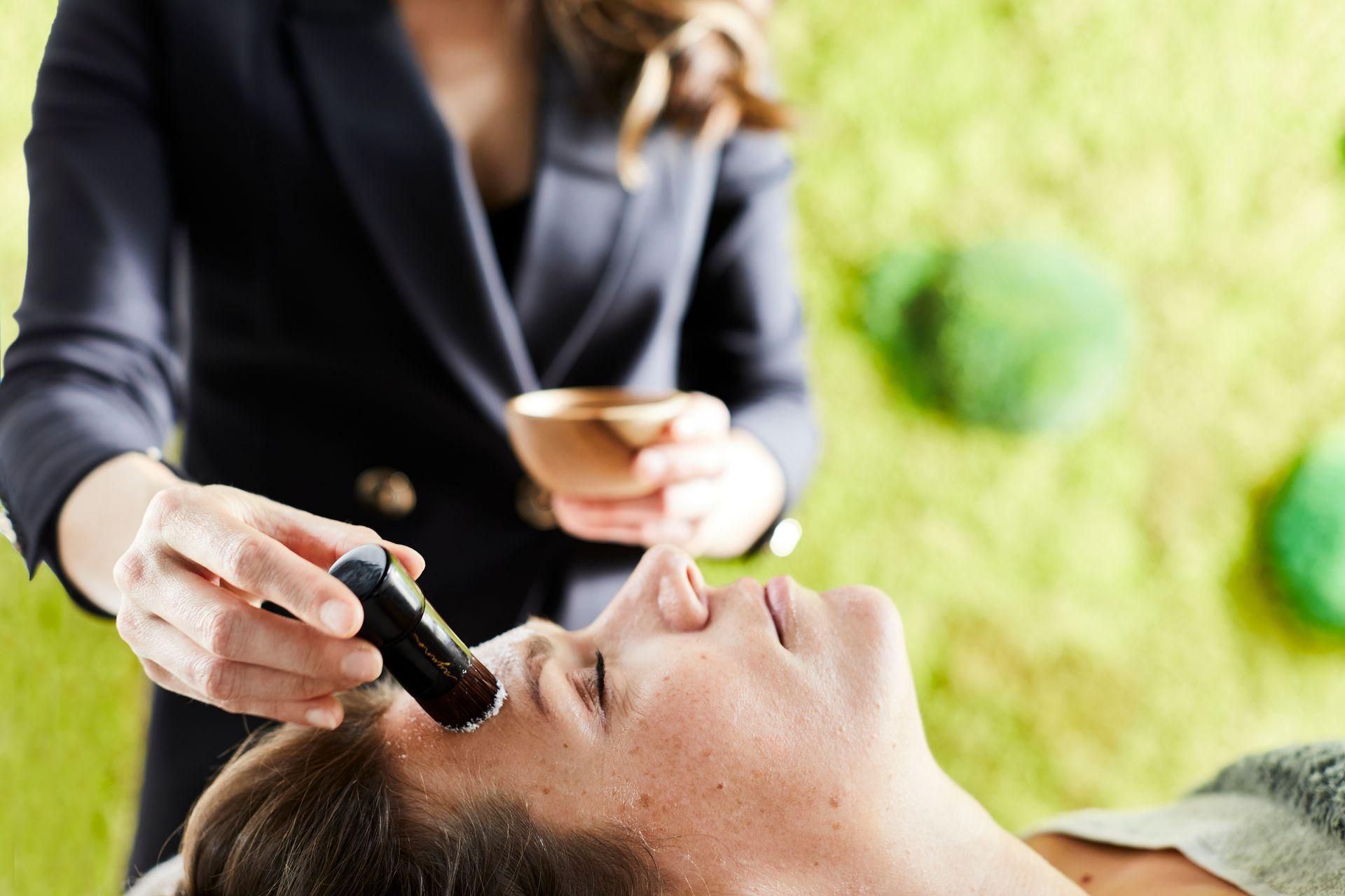 Visagiste brengt oogmake-up aan bij een liggende klant in de buitenlucht.