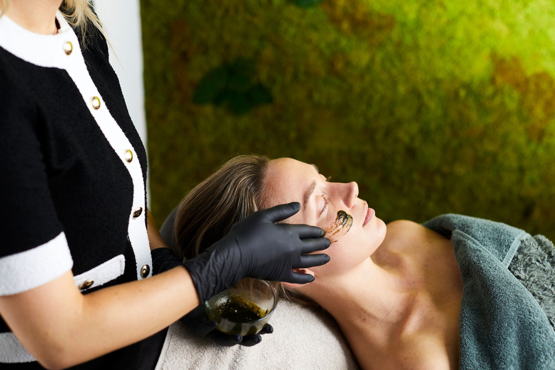 Een spa-therapeut geeft een gezichtsbehandeling aan een liggende klant in een serene omgeving.