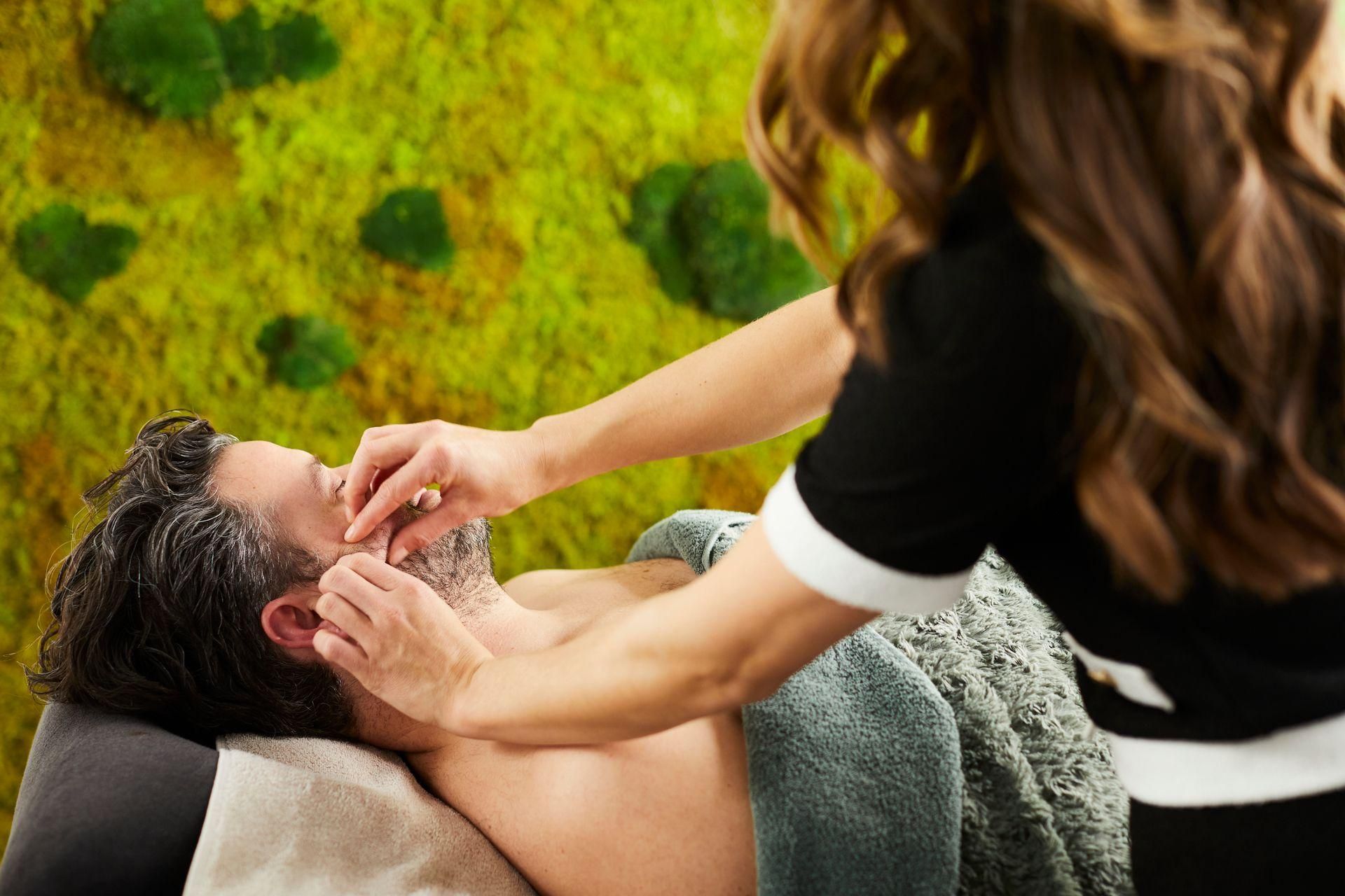 Persoon krijgt buiten een schoudermassage, liggend op een handdoek met een groene achtergrond.