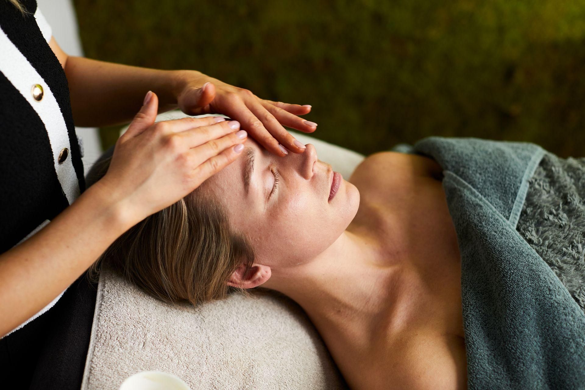 Een spa-therapeut masseert het voorhoofd van een ontspannen cliënt op een behandeltafel.