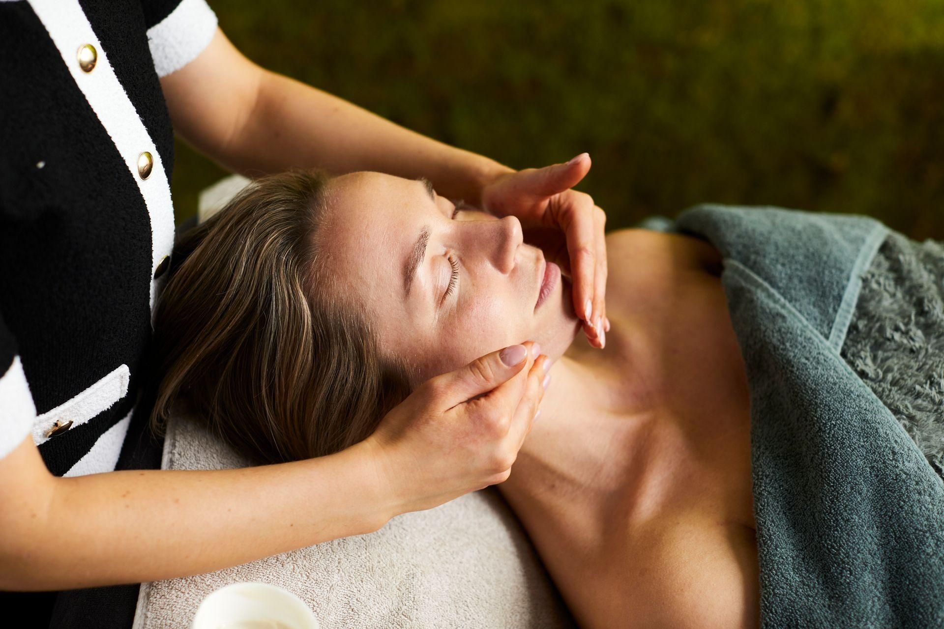 Een spa-therapeut geeft een gezichtsmassage aan een ontspannen klant op een behandeltafel.