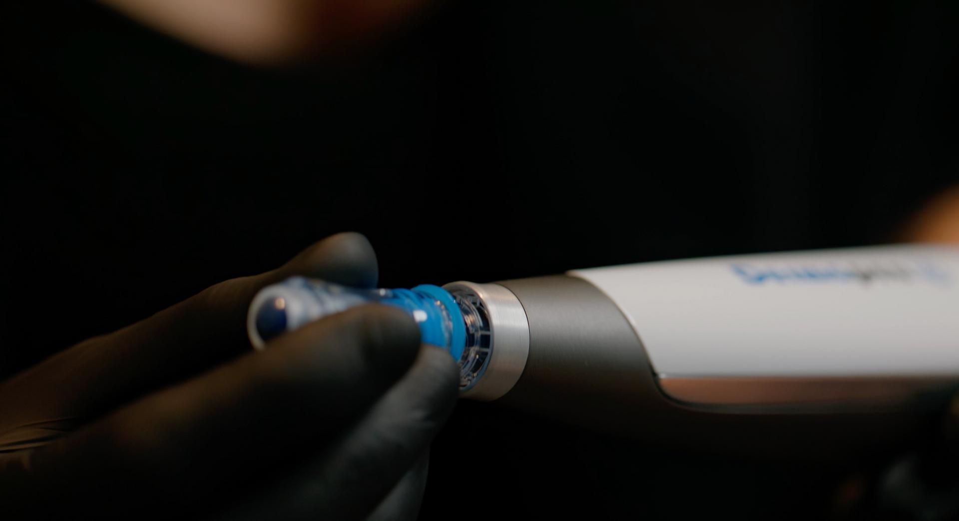 Hand met handschoen die een blauw-witte pen vasthoudt in een donkere omgeving.