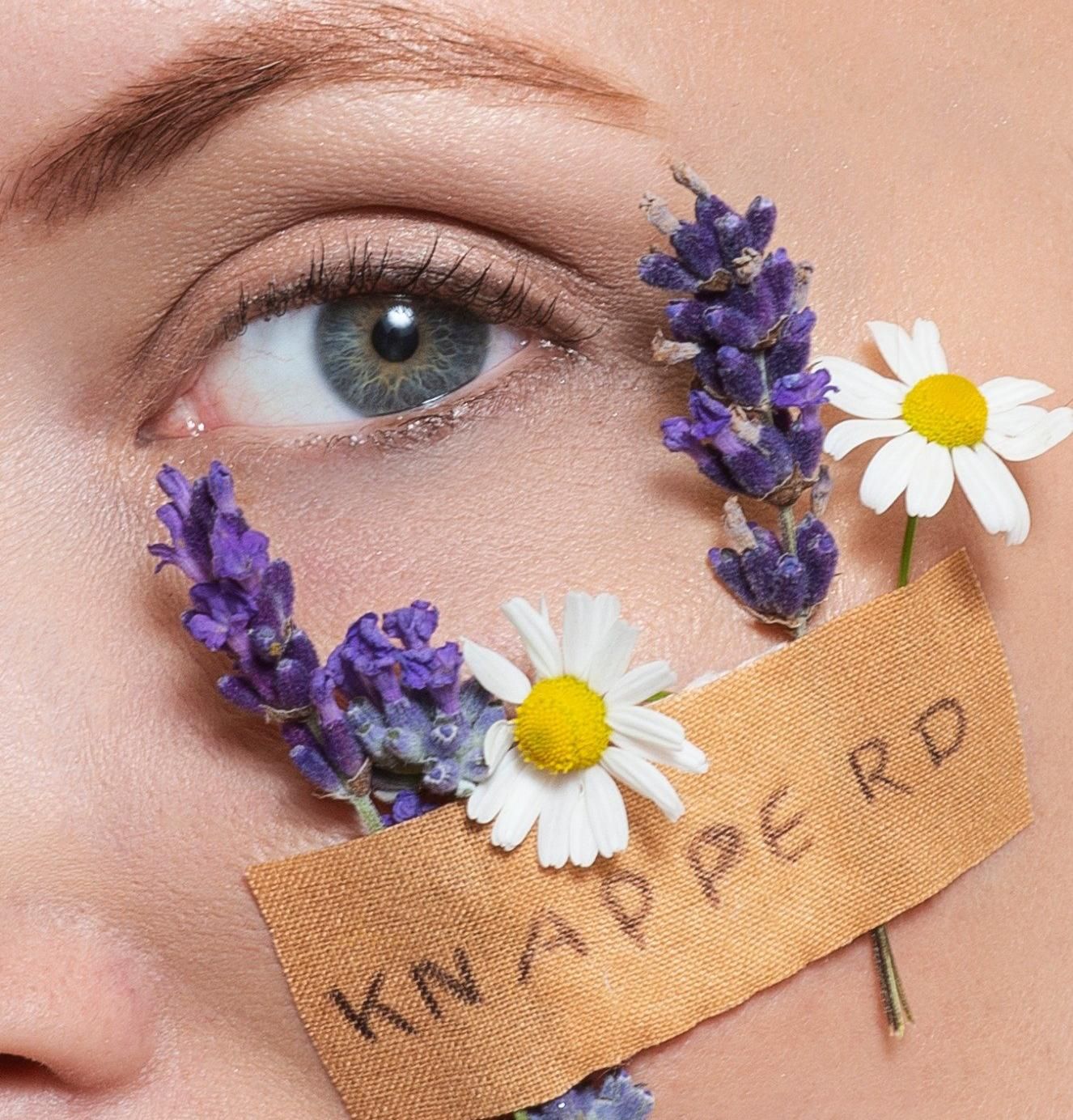 Close-up van een gezicht met paarse bloemen en madeliefjes rond het oog, met 