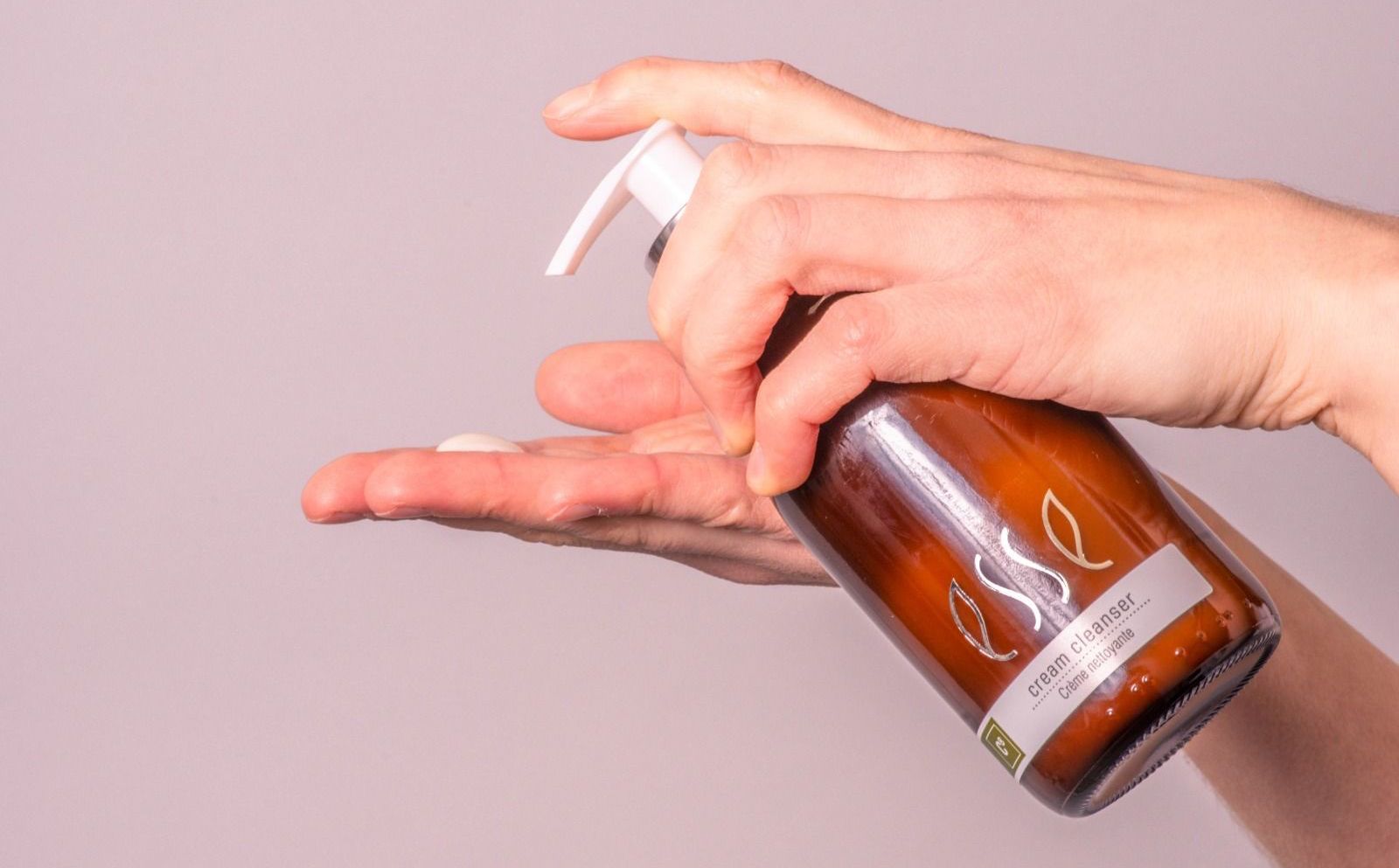 De hand brengt oranje vloeibare zeep uit een bruine pompflacon aan op een open handpalm.
