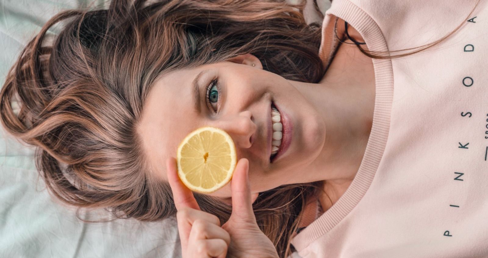 Lachende vrouw met een schijfje citroen voor één oog, liggend op een lichte ondergrond.