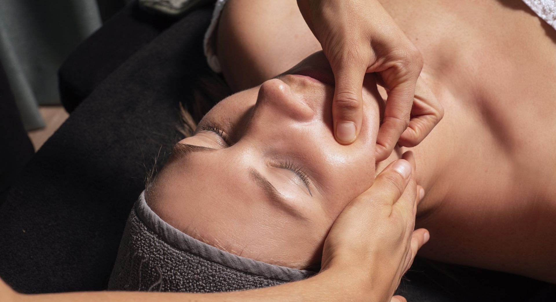 Close-up van een persoon die een gezichtsmassage krijgt, waarbij vingers rond de ogen en neus drukken.