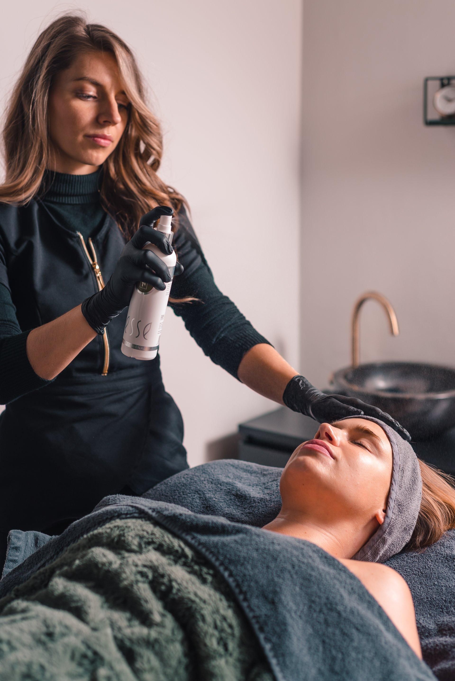 Een spa-medewerker voert een behandeling uit bij een cliënt die op een bed ligt in een serene behandelkamer.