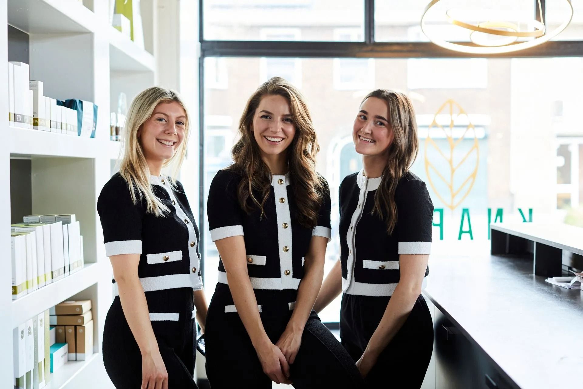 Drie vrouwen in zwart-witte uniformen glimlachen in een lichte, moderne receptie.