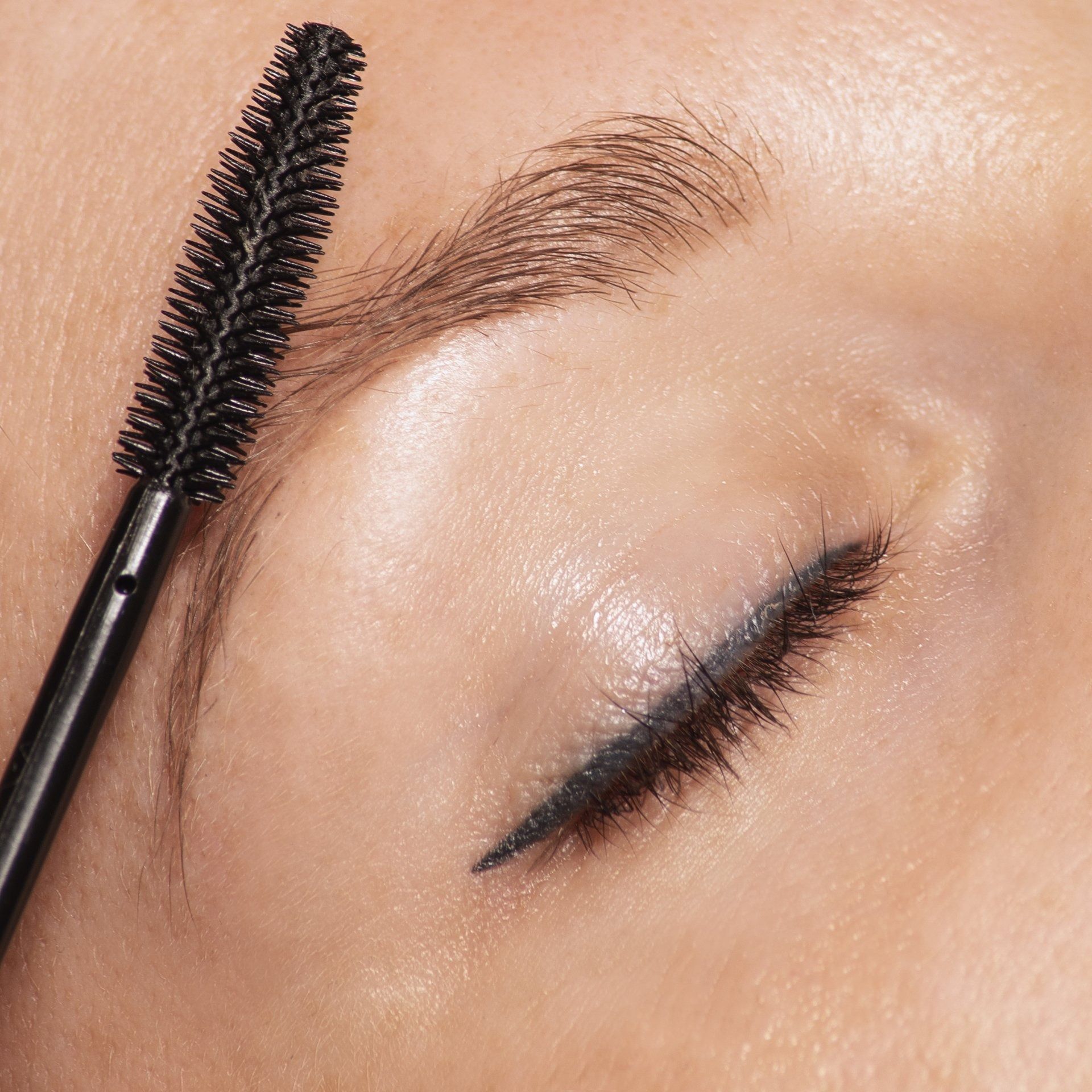 Close-up van een oog met een mascaraborsteltje waarmee zwarte mascara op de wimpers wordt aangebracht.