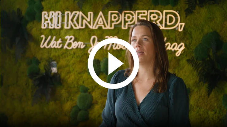 Een vrouw spreekt voor een achtergrond van groen gebladerte, met grote tekst en een afspeelknop eroverheen.