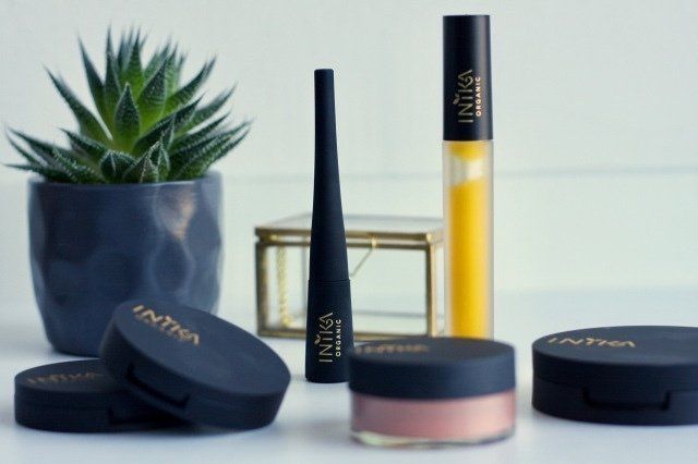 Cosmetica tentoongesteld met een potplant, waaronder zwart-gouden tubes en ronde compacte doosjes op een lichte ondergrond.