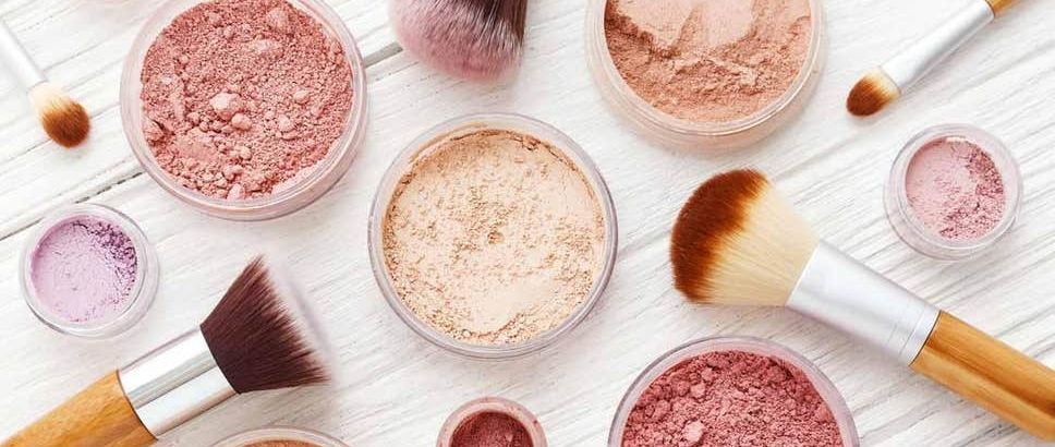 Diverse roze en beige make-uppoeders met make-upkwasten op een witte ondergrond.