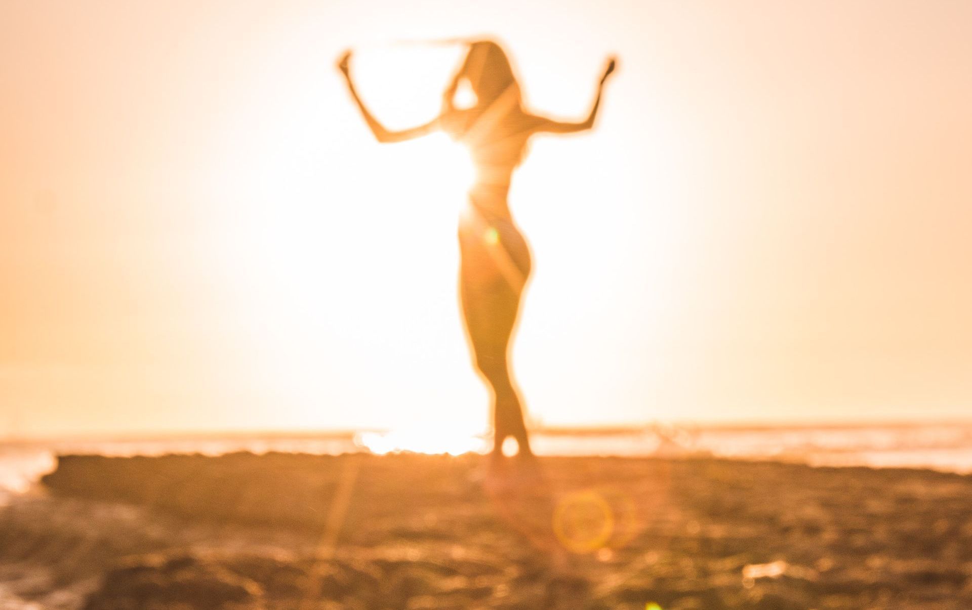 Silhouet van een persoon die danst bij zonsondergang op een zandstrand, in warm goudkleurig licht.