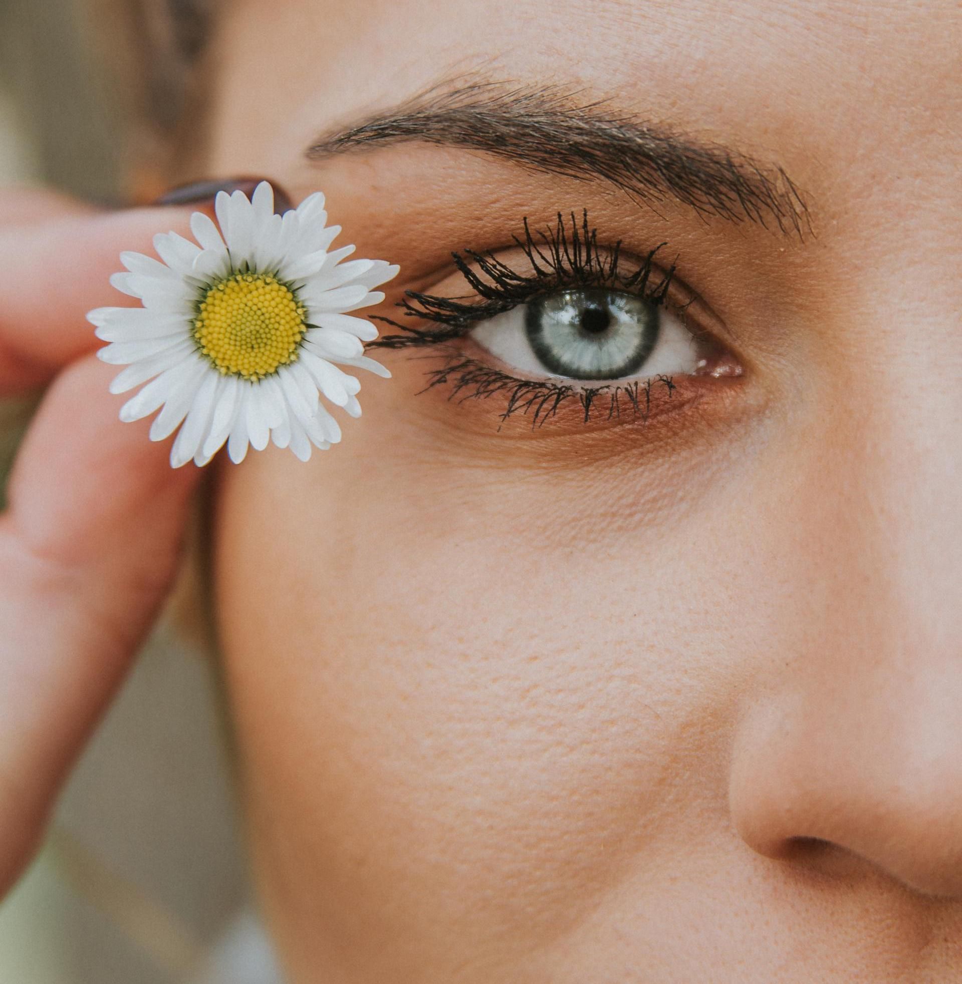 Close-up van een oog met een witte margriet ernaast.