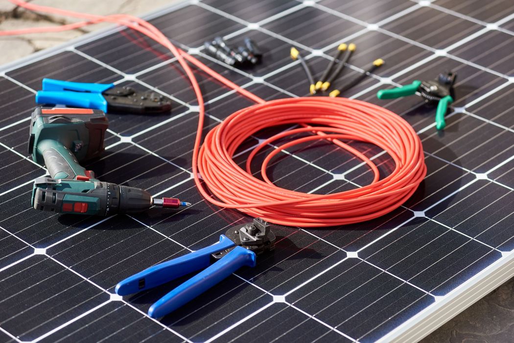Pannello solare con bobina di cavo rosso e utensili elettrici sopra.