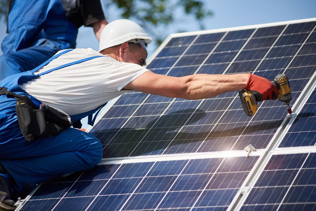 Operaio che installa pannelli solari su un tetto con un trapano elettrico.