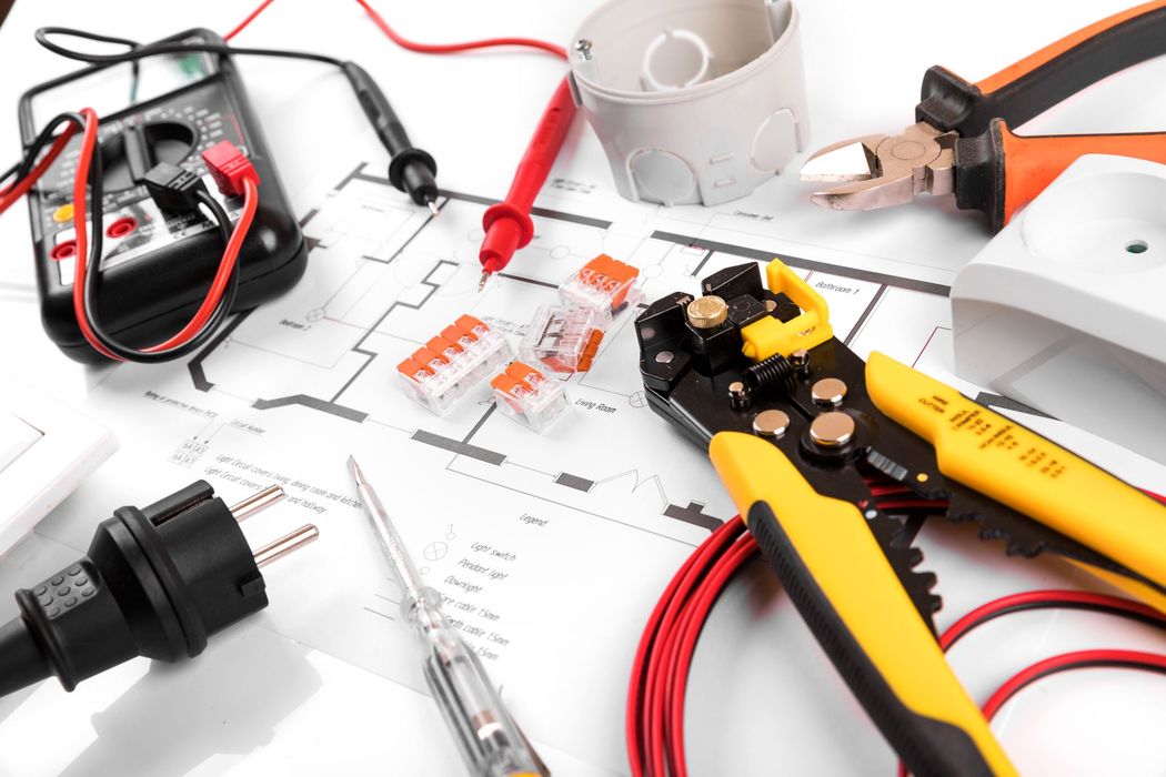 Attrezzi elettrici e cablaggi su un banco da lavoro bianco, tra cui pinze, cavi e connettori.