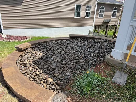 Rock garden with dark stones beside a curved tan retaining wall and a house exterior