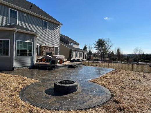 Backyard patio with a circular fire pit beside a gray house on a sunny day