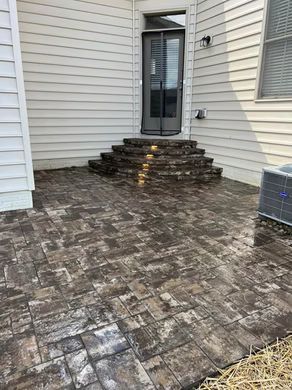 Brick patio and stone steps leading to a black door between beige house walls