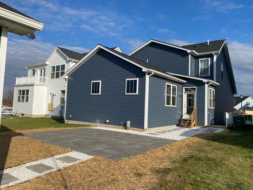 Blue house with white trim and a small front porch beside a lawn and paved walkway.