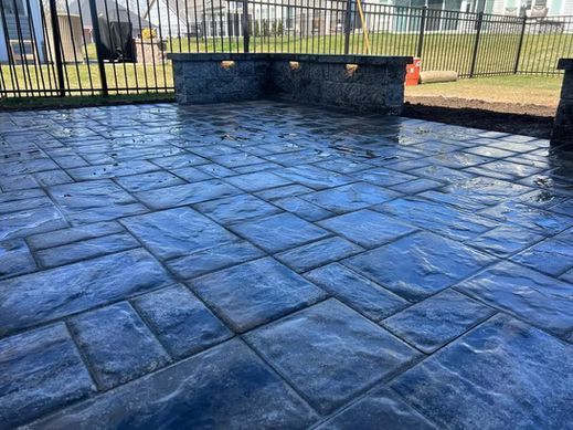 Blue stamped concrete patio with stone seating wall and black metal fence in the background