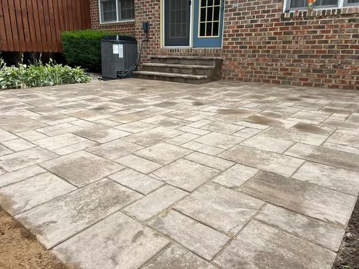 Stone patio beside a brick house with a blue door and steps, with a utility box near the wall