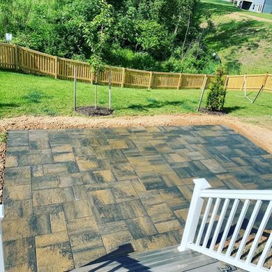 Back patio with tan pavers, white railing, and a grassy yard with wooden fence and trees beyond