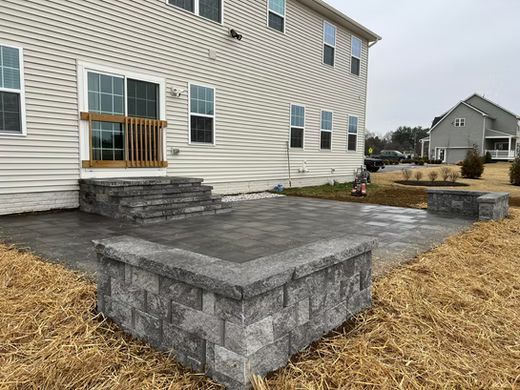 Stone patio with raised seating walls beside a beige house and small deck.
