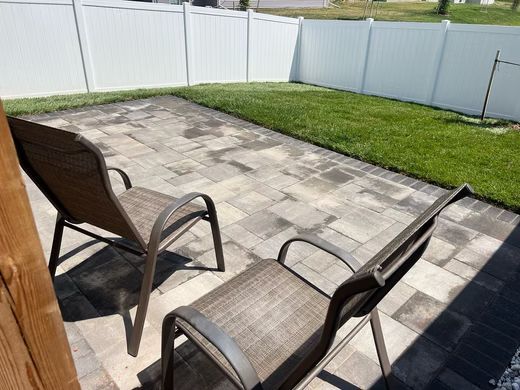 Patio with two lounge chairs, stone pavers, green grass, and a white fenced backyard